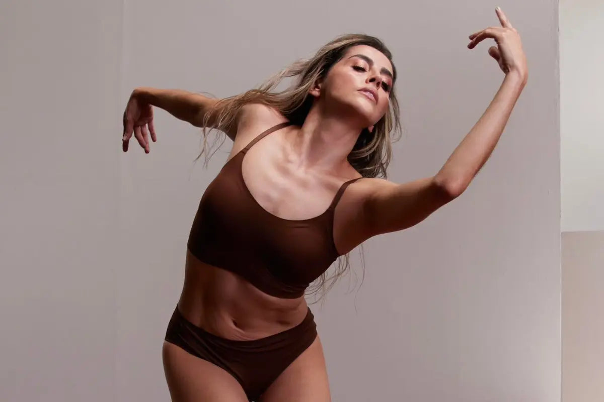 Seamless bralette in chocolate brown worn by a model in a graceful dance pose against a neutral background.