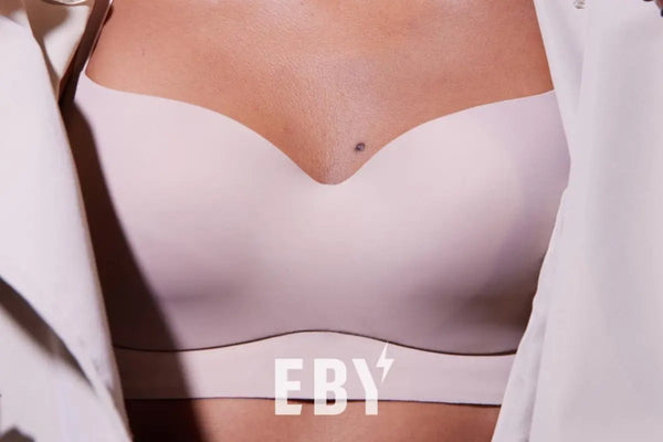 Close-up of an EBY wireless bralette in pale blush with a sweetheart neckline, worn under an open white shirt in soft natural light.
