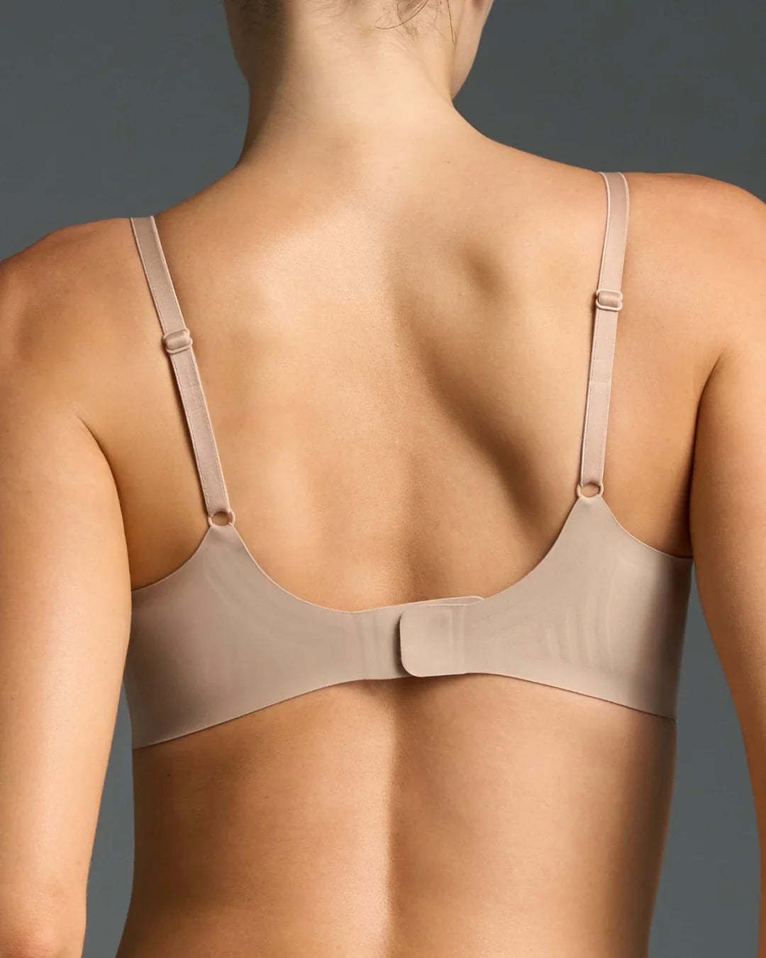 Wireless nude bra with thin adjustable straps, scoop back, and seamless hook closure, rear view.