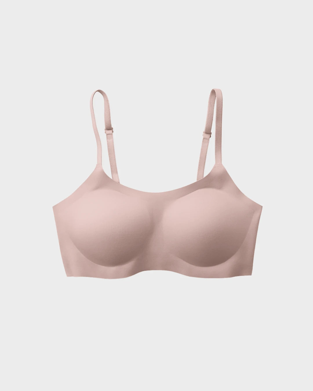 Blush pink seamless scoop-neck bralette with adjustable straps and molded cups laid flat on a light gray background.