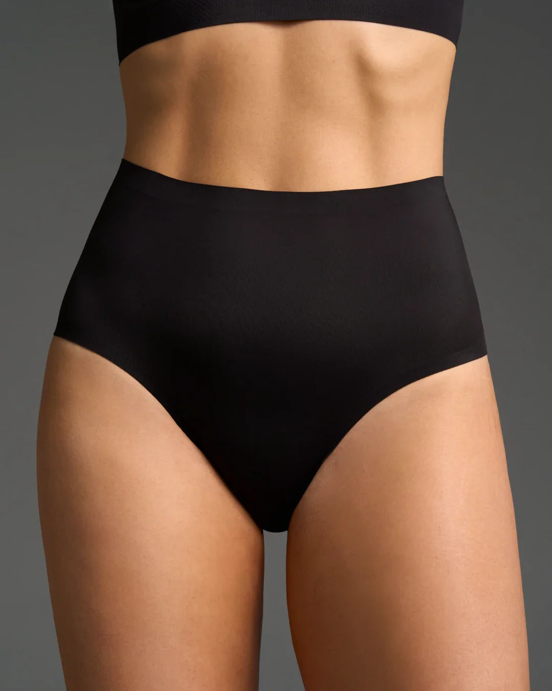 Seamless high waisted panties in black with smooth waistband modeled against a dark background