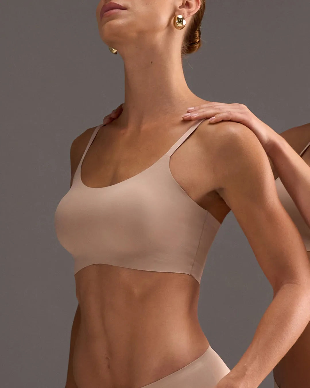 Woman wearing a nude support  bralette against a neutral background